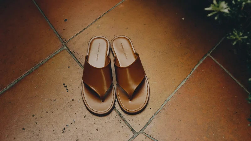 Paire de sandales plates en cuir sur du carrelage en terre cuite.