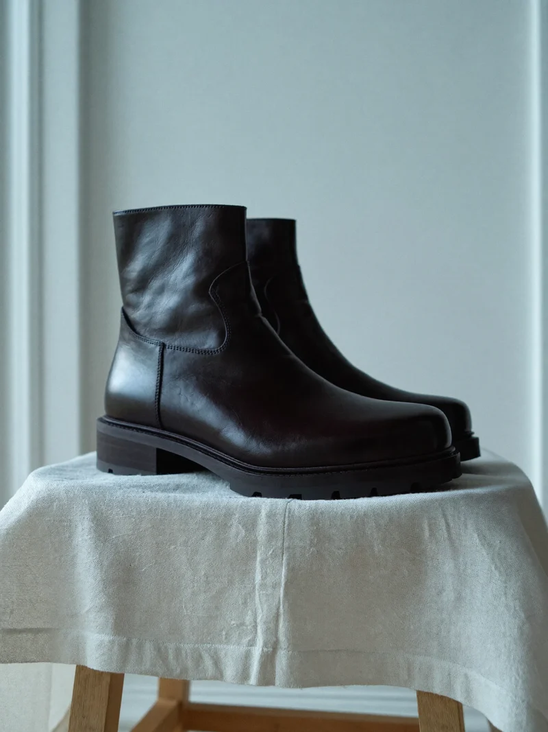 Paire de bottines en cuir sombre posée sur un tissu de lin.